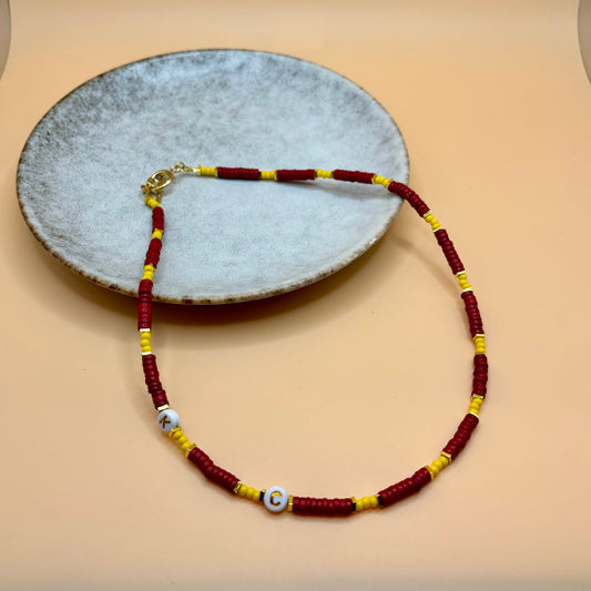 A Kansas City Chiefs inspired necklace of red, golden yellow, and gold beads lies draped on a dish.